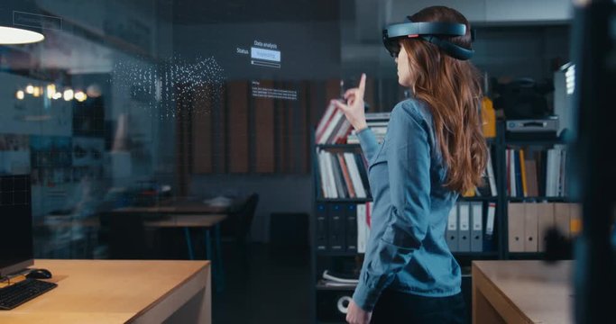 Young adult female using holographic augmented reality glasses in trendy office. Future concept. Generic big data interface added 