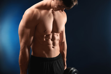 Fototapeta na wymiar Muscular bodybuilder with dumbbell on dark background