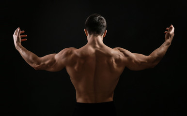 Muscular bodybuilder on dark background, back view