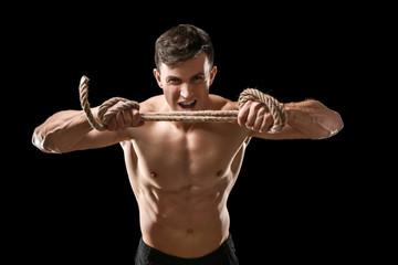 Muscular bodybuilder with rope on dark background
