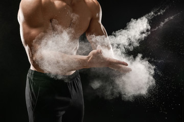 Young sporty man applying talc on hands against dark background