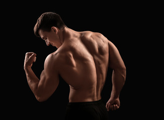Muscular bodybuilder on dark background, back view