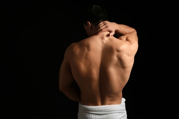 Muscular sexy bodybuilder with towel on dark background, back view