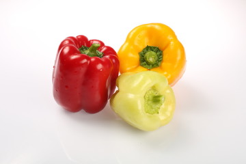 Three delicious ripe Bulgarian peppers, lime, red, orange, with green tails in the same plane on a white background