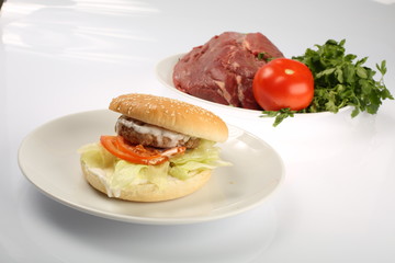 cheeseburger with bacon and beef patty on a plate with vegetables, bell pepper, tomatoes, onions, cucumber, parsley and salad on a white background