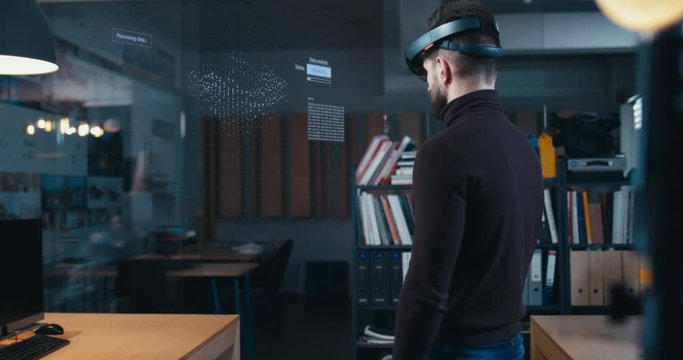 Young adult Caucasian male using holographic augmented reality glasses in trendy office. Future concept. Generic big data interface added