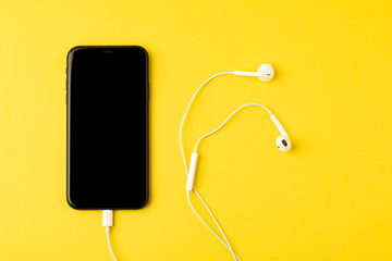 Obraz premium Smartphone with headphones on yellow background. The view from the top. Listen to music.
