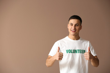 Young male volunteer showing thumb-up on color background