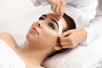 Young woman undergoing eyebrow correction procedure in beauty salon