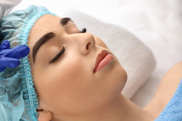 Fototapeta na wymiar Young woman undergoing eyebrow correction procedure in beauty salon