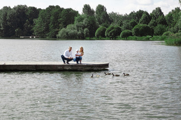 Fototapeta na wymiar young family feeds wild ducks sitting on a pier by the lake