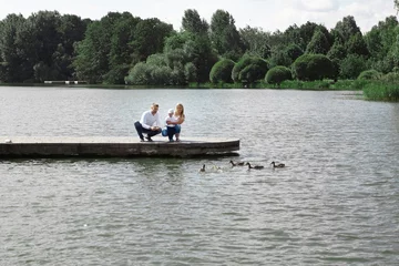 Foto op Canvas young family feeds wild ducks sitting on a pier by the lake © yurolaitsalbert