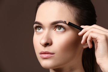 Young woman undergoing eyebrow correction procedure on color background