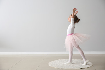 Cute little ballerina dancing near light wall