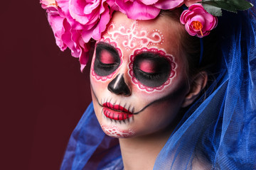 Young woman with painted skull on her face for Mexico's Day of the Dead against color background