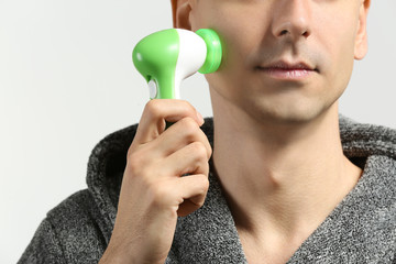 Man with facial massage tool on light background, closeup