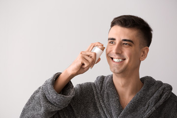 Handsome man applying face serum on light background