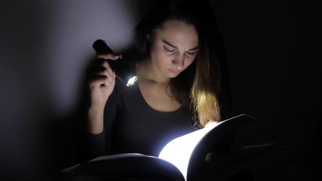 close-up portrait girl is reading a book with a flashlight in a dark room at night. 4k. Motion shooting
