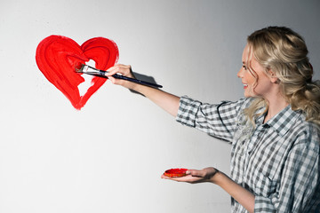 Young woman in plaid shirt with paintbrush is drawing a heart on the wall