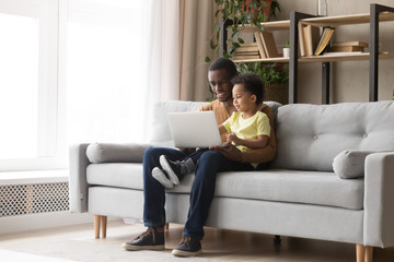 Young black father and kid son using laptop at home