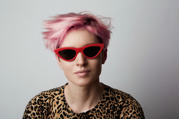 Fashion Portrait of young Fabulous trendy woman with red sunglasses and pink short hair poising at camera over white empty background