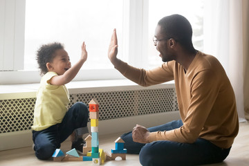 Happy black dad and toddler son giving high-five playing together