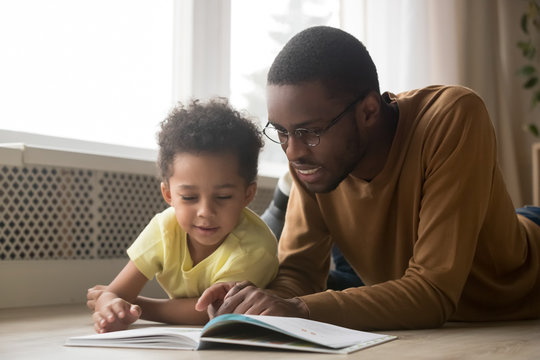 Happy black father and toddler son reading book at home