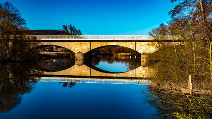 Fototapeta premium Winter landscape, Marburg, Germany - A beautiful reflection of the old land bridge of the B3, over the Lahn, in Argenstein near Weimar. On a day in February with cloudless blue sky.