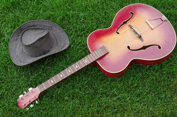 Acoustic guitar and cowboy hat on the grass