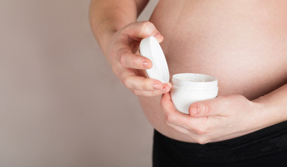 Fototapeta na wymiar Young pregnant woman keeps skin cream care close to her belly.