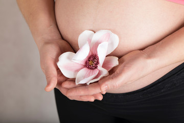 Young pregnant woman keeps artificial orchid flower close to her belly.