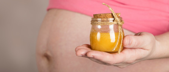 Young pregnant woman keeps glass bottle of natural honey.