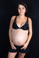 Isolated portrait of beautiful smiling young woman in dress waiting for baby in black background