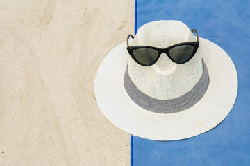 top view of sandy beach with towel frame and white hat with sunglasses