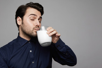 Young confident man holding hand glass of fresh milk on gray background.