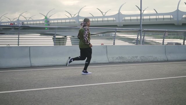 Portrait of african american man jogging on road bridge. Runner in sportswear working out alone aving cardio challenge, preparing for triatlon race.