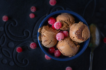 Balls of chocolate ice cream and red currant berries touched by frost in a blue bowl on a dark surface. Low key photography (dark-colored), soft focus.