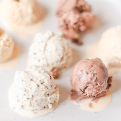 Melting balls of chocolate, caramel, vanilla ice cream on a light surface. Llight square blurred background. Sweet food, treat.