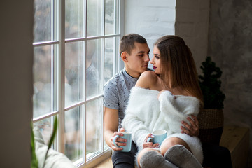 beautiful girl and guy sit on the windowsill near the window with a cup of tea and look at each other