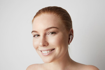Portrait of charming redhead woman with happy smile listening music with wireless earphone in ear