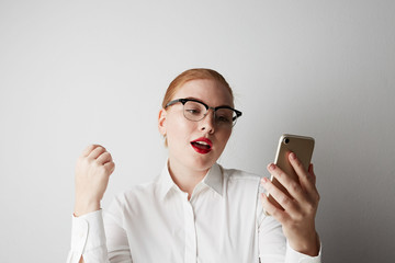 Beautiful redhead woman using mobile phone at office over gray background