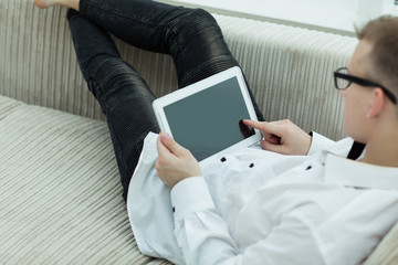 side view. modern guy reading an e-book sitting on the couch of his living room