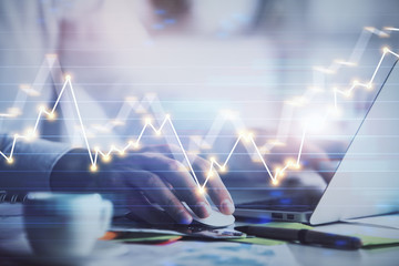 Hands typing on laptop. Business and Financial concept. Double exposure of stock market charts.