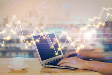 Hands typing on laptop. Business and Financial concept. Double exposure of stock market charts.