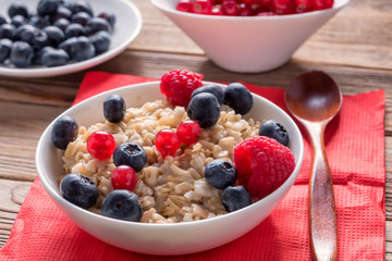 Close up view of porridge with blueberries and raspberries and grain bread on wooden background. Healthy breakfast.