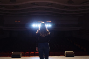 the unrecognizable girl singing on the stage in front of the spotlight, back view