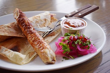 Delicious kebab with sauce and red onions on a white plate.