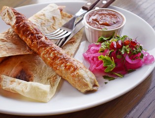 Delicious kebab with sauce and red onions on a white plate.