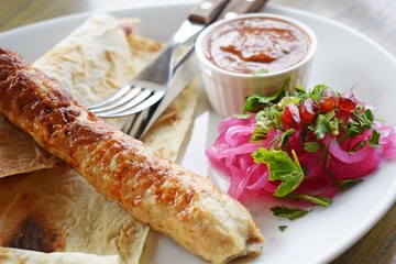 Delicious kebab with sauce and red onions on a white plate.