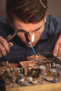 Jeweller crafting on a wooden work bench with a blowpipe